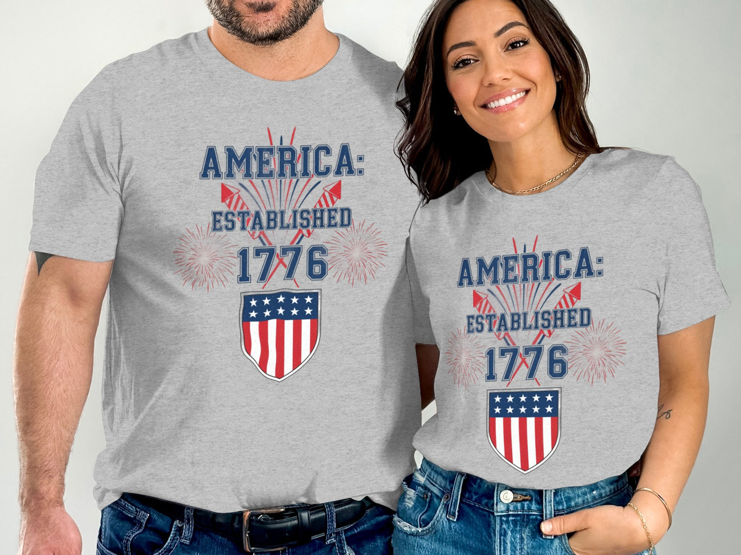 Two people wear gray t-shirts with "America: Established 1776" and a shield graphic.