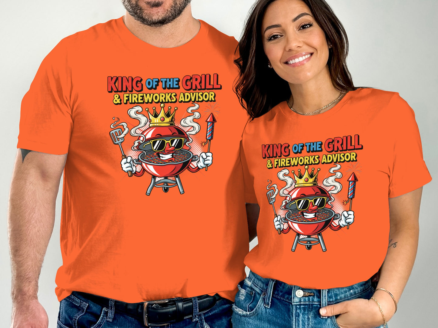 Couple in matching orange t-shirts with "King of the Grill & Fireworks Advisor" text and cartoon grill graphic.