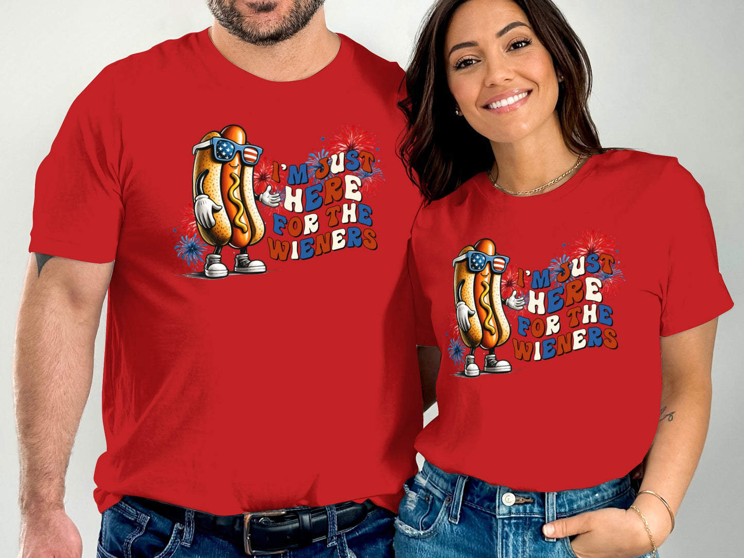 Two people wear matching red t-shirts with cartoon hot dogs and "I'm just here for the wieners."