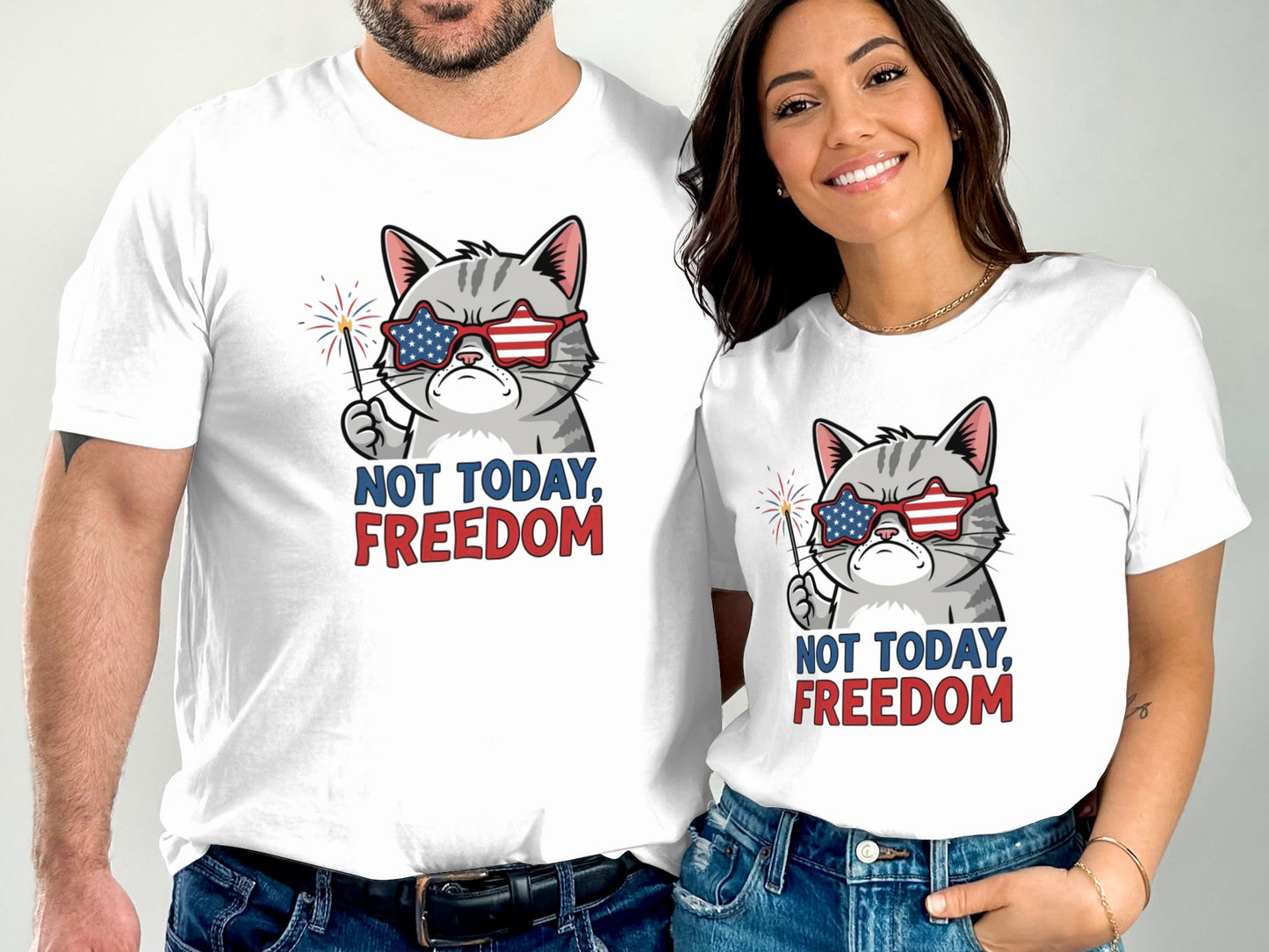 Two people wear white t-shirts featuring a cartoon cat wearing sunglasses and holding a sparkler, with text "NOT TODAY, FREEDOM".