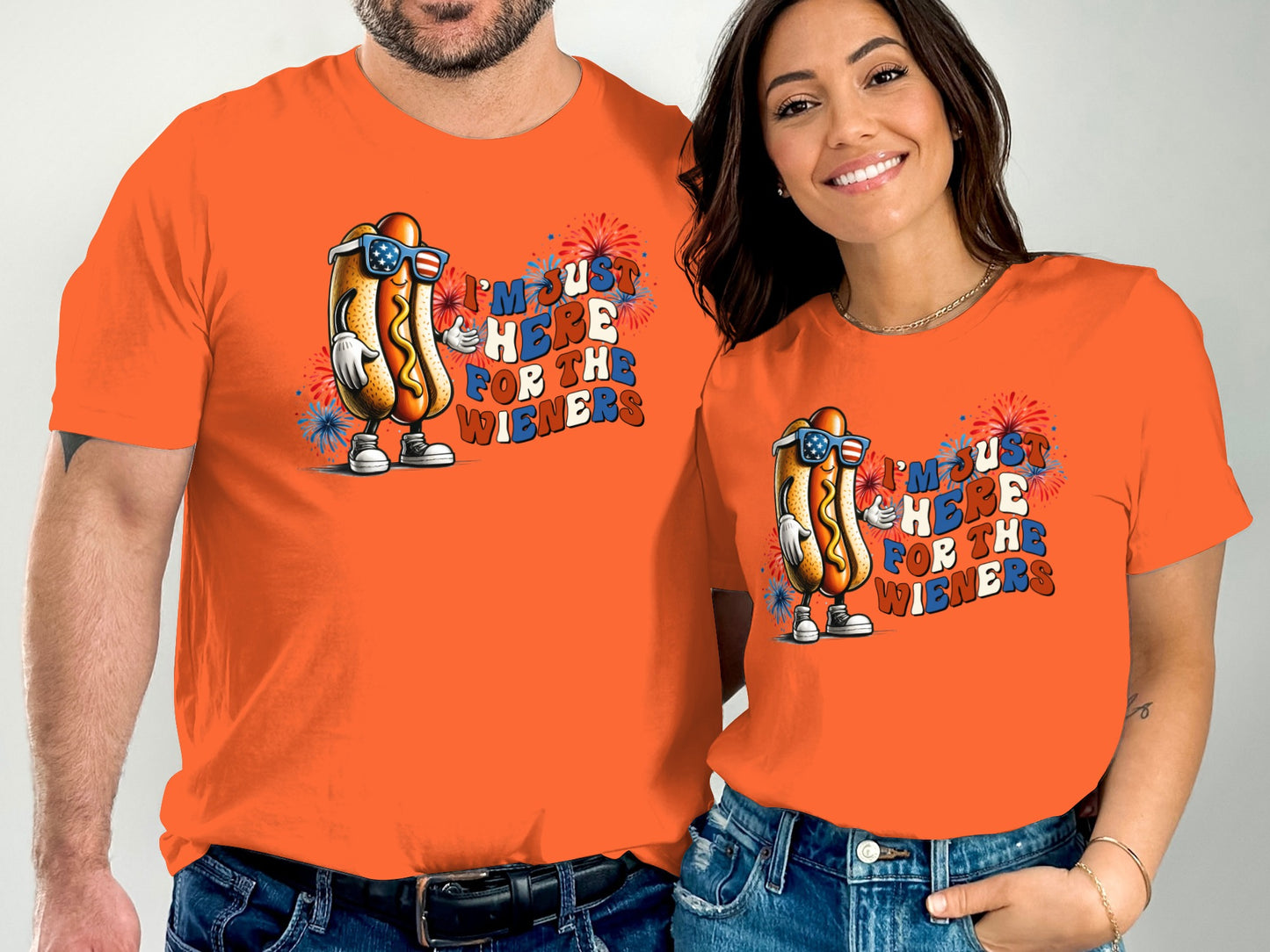 Couple wearing matching orange t-shirts with patriotic hot dog graphic.