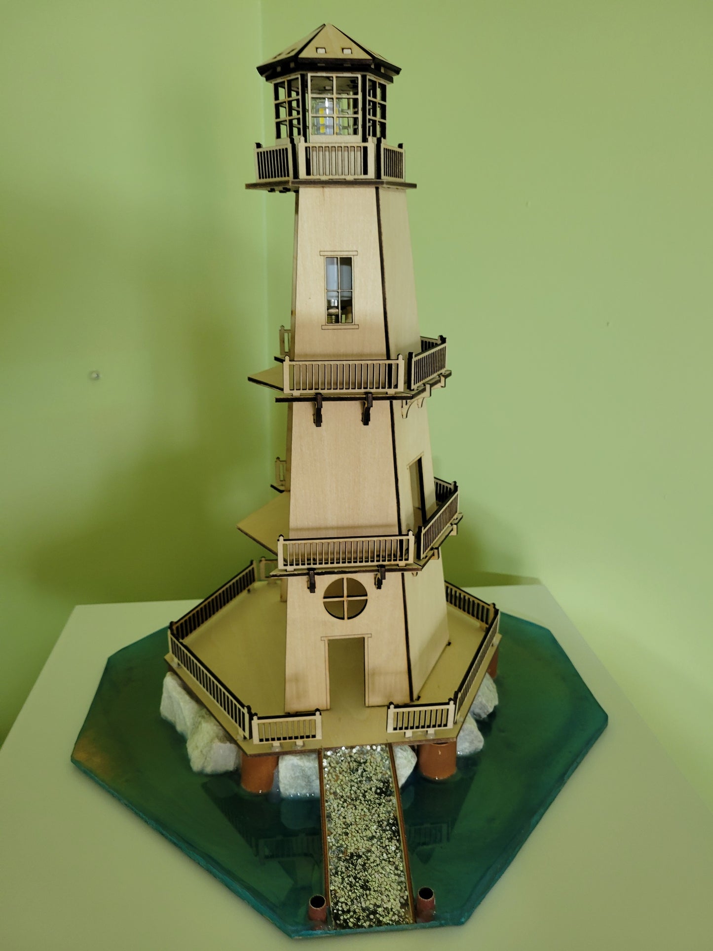 Laser-cut wooden model of a lighthouse with intricate details and a scenic base.