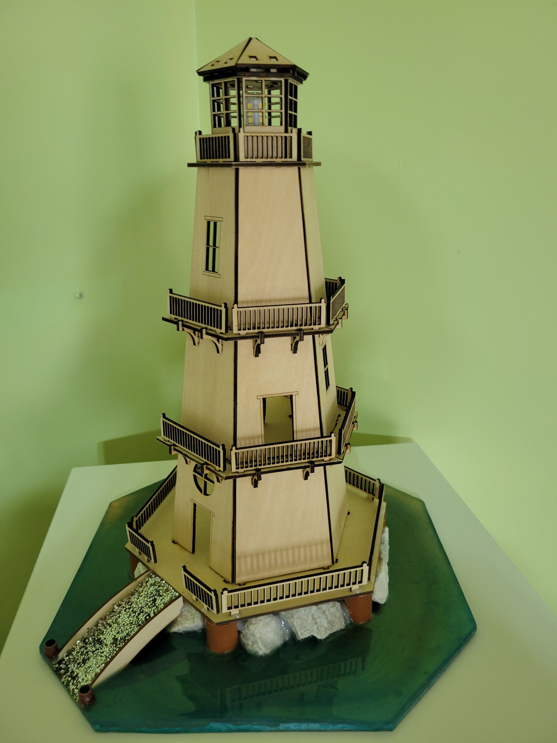 Wooden lighthouse model featuring intricate railings, balconies, and a simulated rocky base with water.