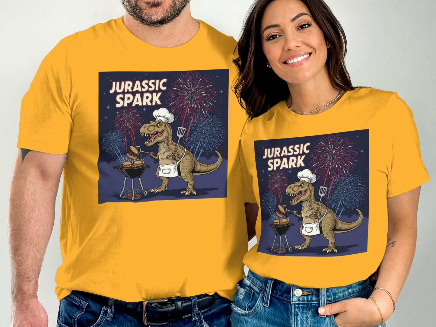Couple wearing matching "Jurassic Spark" t-shirts with a grilling dinosaur graphic.
