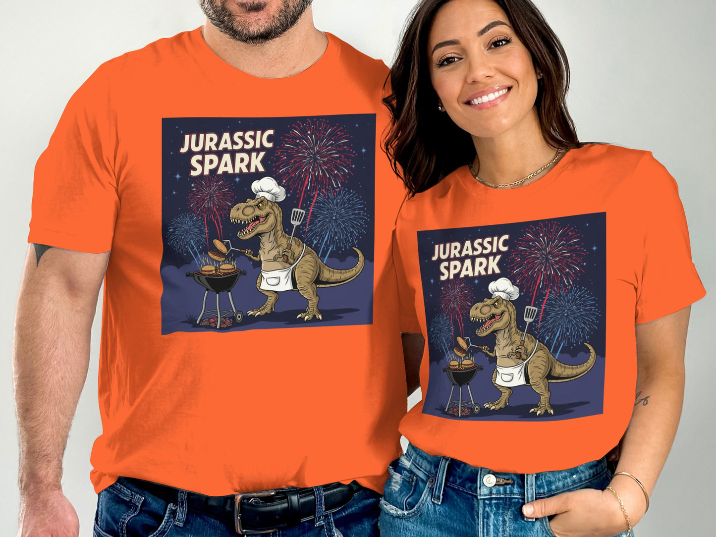 Couple in orange Jurassic Spark t-shirts grilling a dinosaur with fireworks.