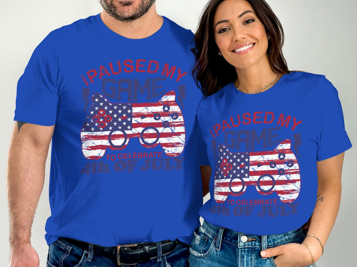 Two people wearing matching blue t-shirts with an American flag controller design and "PAUSED MY GAME 4TH OF JULY" text.