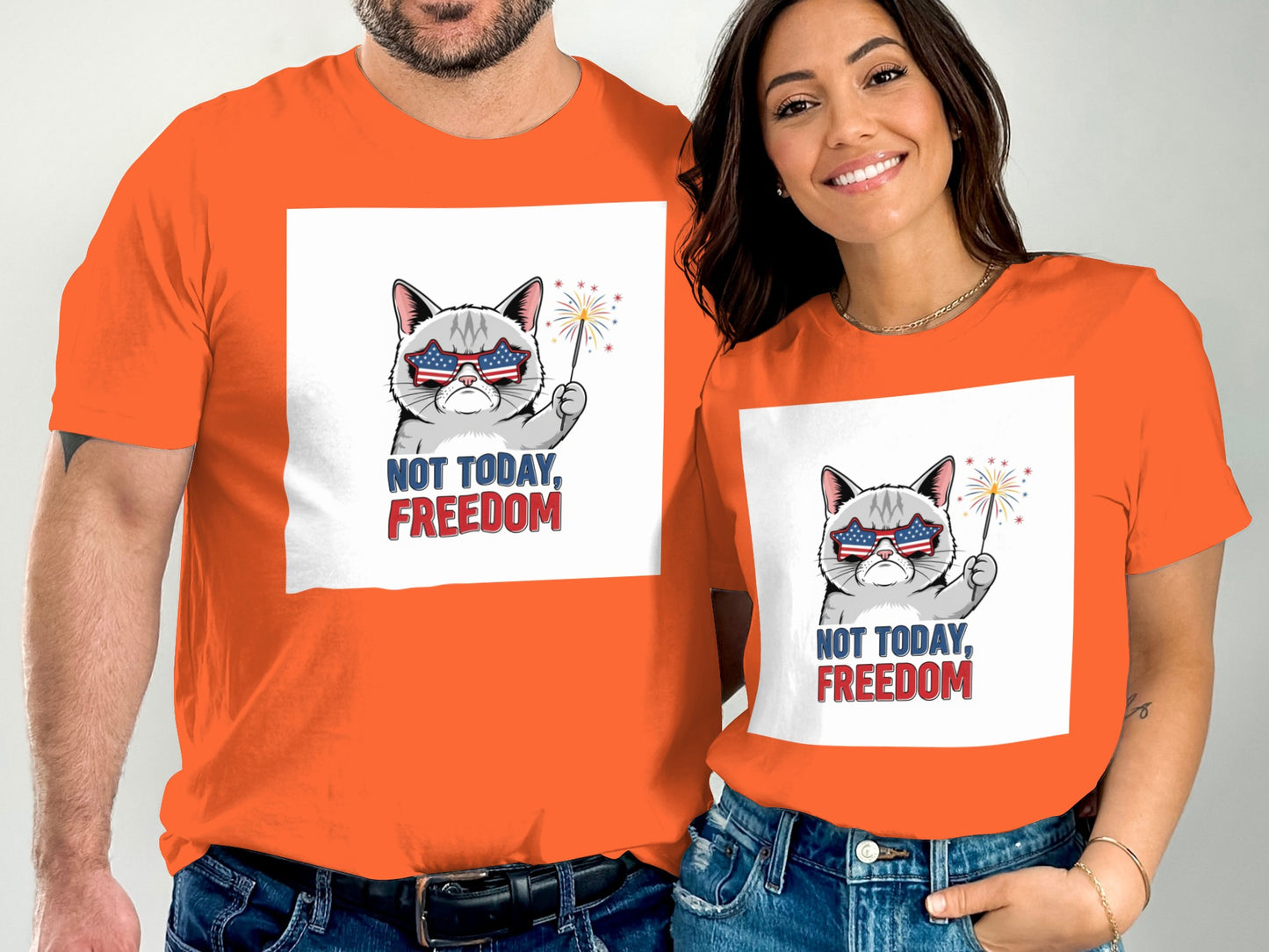 Two people wear orange t-shirts with a patriotic cat graphic and the words "NOT TODAY, FREEDOM".