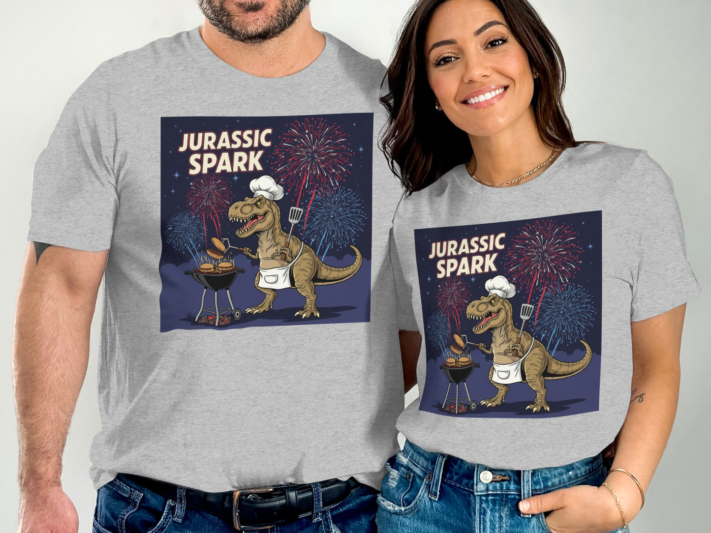 Couple in gray t-shirts with Jurassic Spark dinosaur grilling illustration.