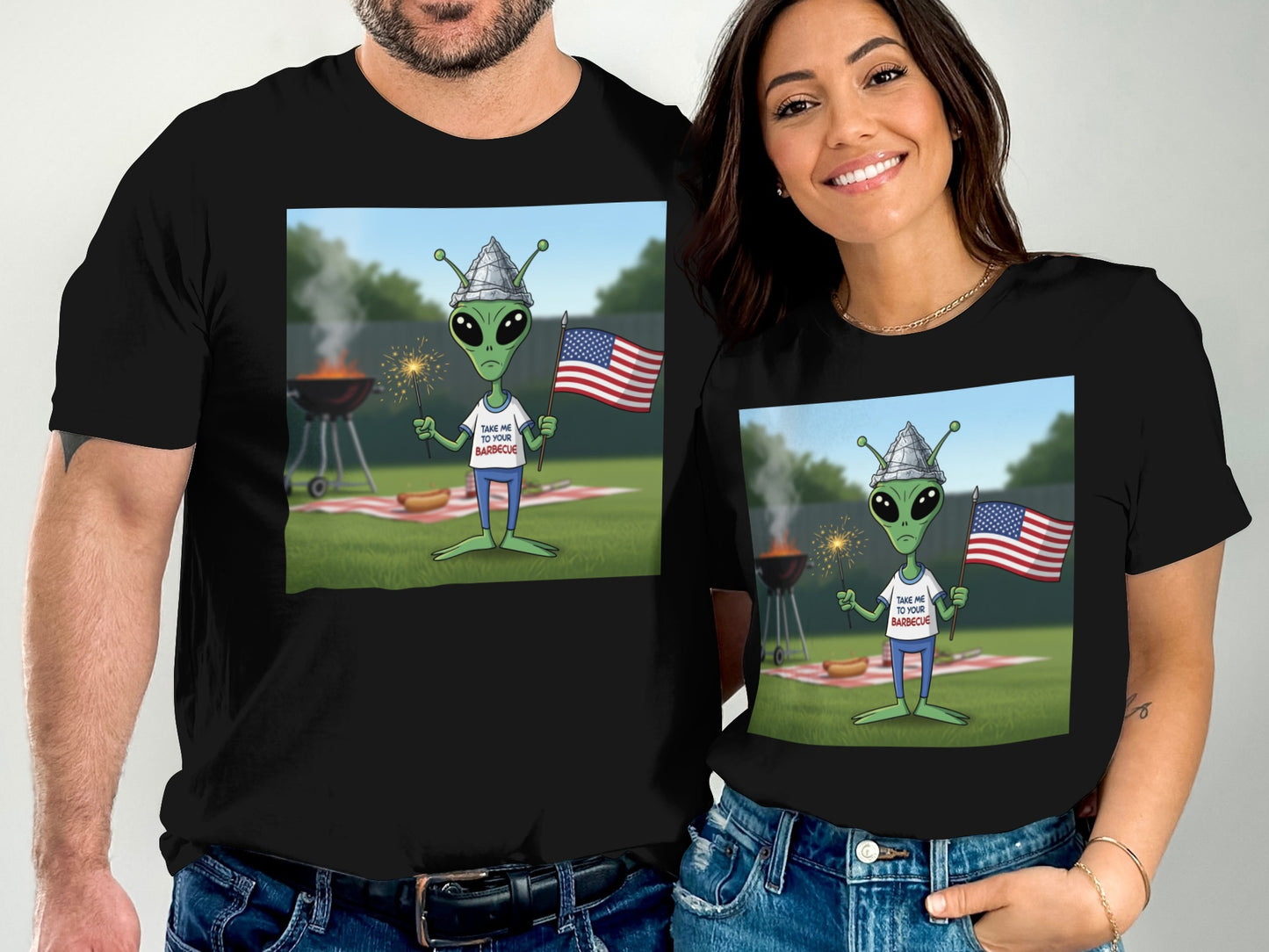 Man and woman wearing matching t-shirts with alien at barbecue graphic.
