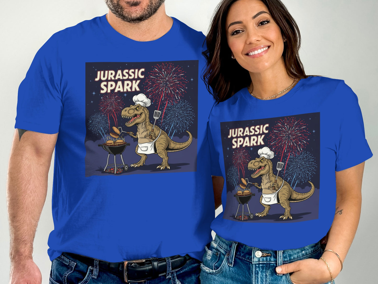 Couple in blue t-shirts with Jurassic Park dinosaur grilling fireworks background.