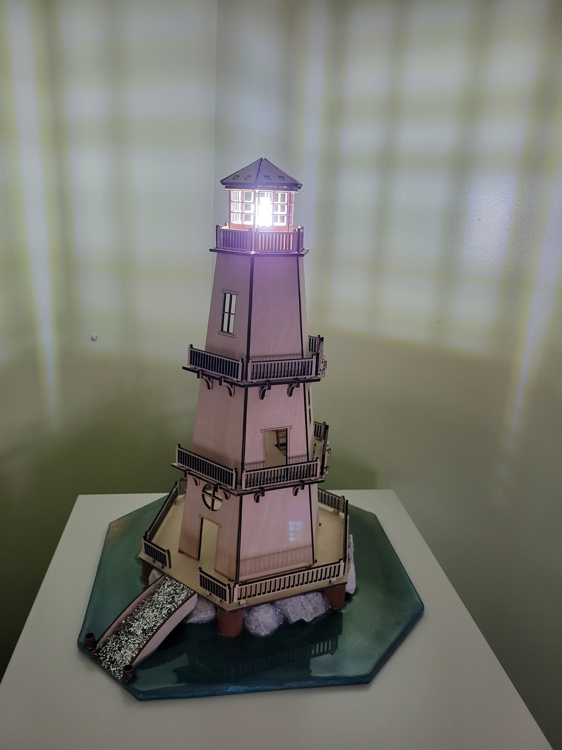 Wooden lighthouse model with illuminated windows and a blue base.