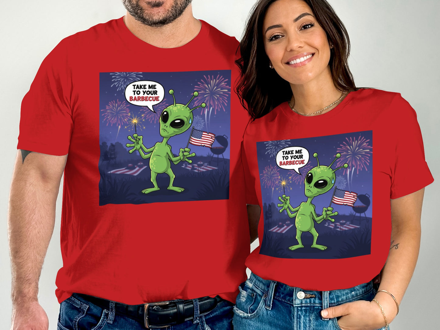 Couple in red t-shirts with alien barbecue design and fireworks.