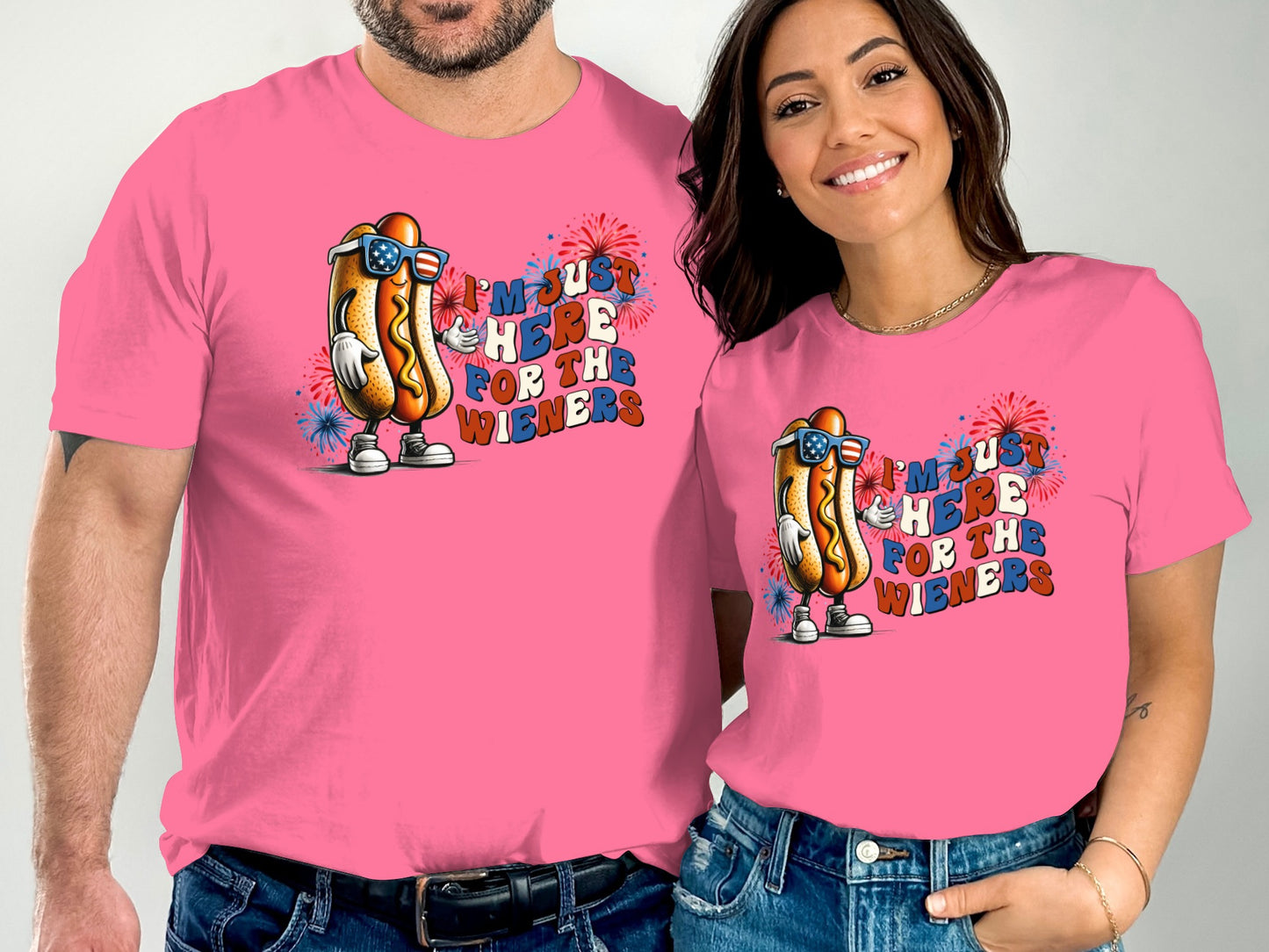 Couple in pink t-shirts with hot dog graphic and "I'm just here for the wieners" text.