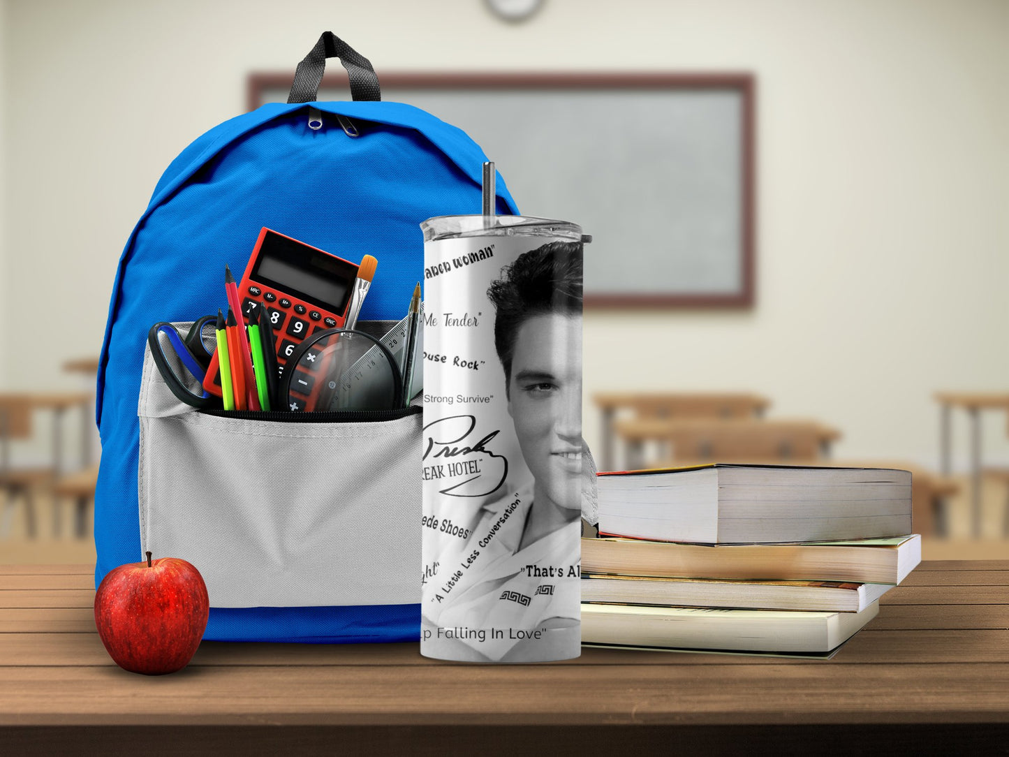 Elvis tumbler gift with black and white design next to a blue backpack, books, and an apple on wooden desk