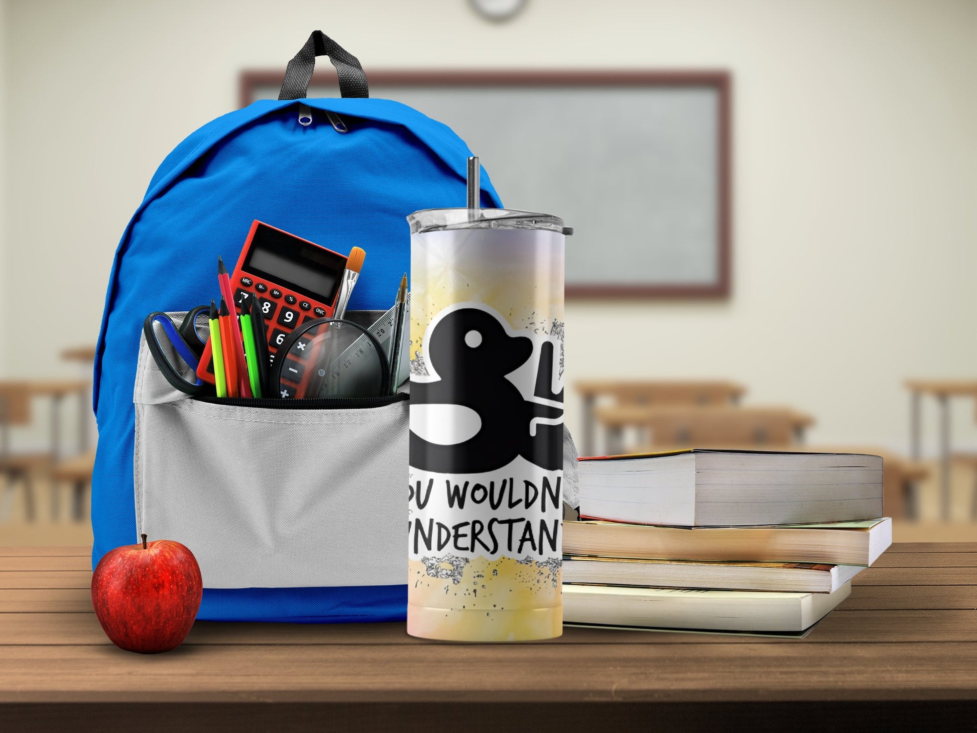 Blue backpack with school supplies and a funny duck tumbler gift on a wooden desk with an apple and books