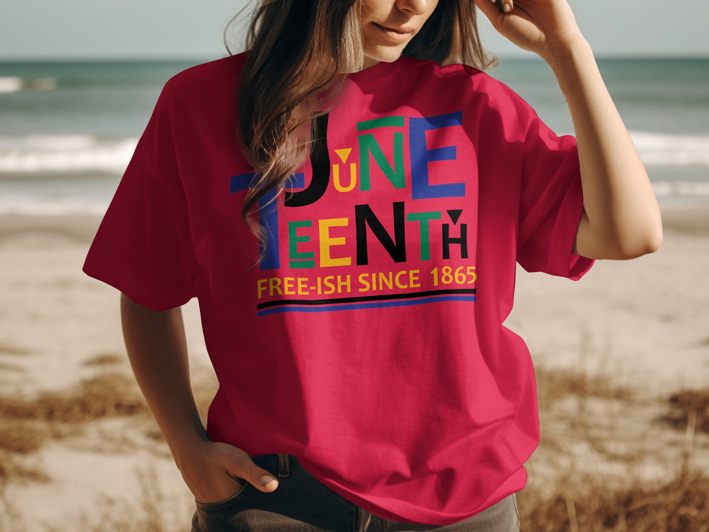Woman wearing a red Juneteenth T-Shirt with colorful text design standing on the beach