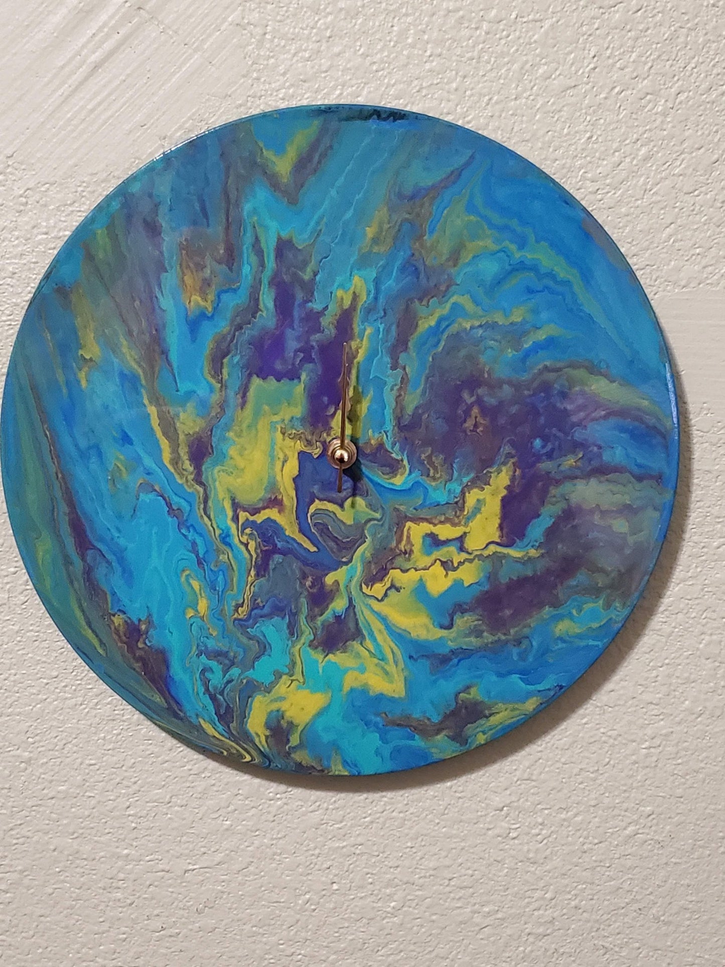 Round handcrafted wall clock with blue yellow and purple abstract swirl design on white wall