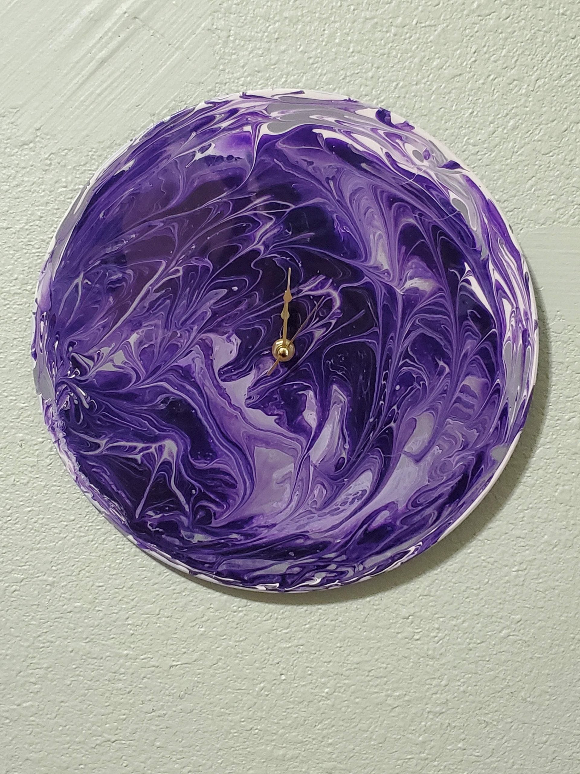 Purple abstract design handmade wall clock decor with gold hands hanging on textured wall